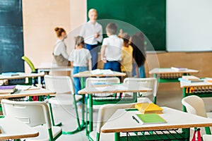 schoolchildren standing around teacher at classroom with desks