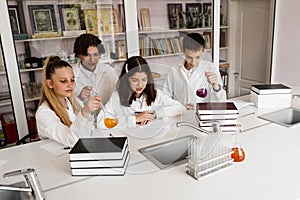 Schoolchildren studying at chemistry lesson in classrom. Pupils writing in notebook, holding flasks with liquid for