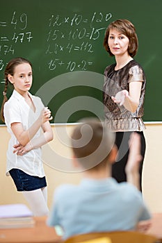 Schoolchildren with teacher in classroom. Pupil solving task standing at blackboard.