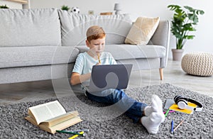 Schooler ginger boy with laptop doing homework at home