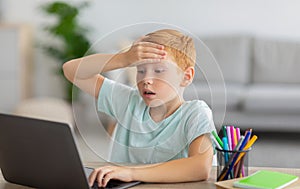 Schooler sitting in front of laptop, touching his forehead