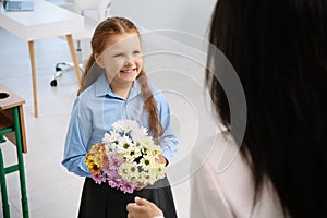 Schoolgirl with bouquet congratulating her pedagogue in classroom. Teacher`s day