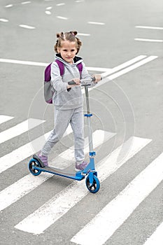 Schoolgirl carrying scooter and crossing road on way to school. Zebra traffic walk way in the city. Pedestrian passing a crosswalk