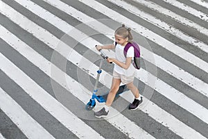 Schoolgirl carrying scooter and crossing road on way to school. Zebra traffic walk way in the city. Pedestrian passing a crosswalk