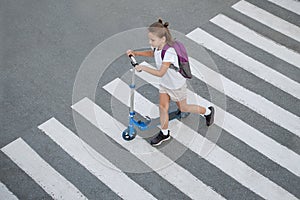 Schoolgirl carrying scooter and crossing road on way to school. Zebra traffic walk way in the city. Pedestrian passing a crosswalk