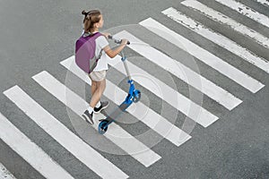 Schoolgirl carrying scooter and crossing road on way to school. Zebra traffic walk way in the city. Pedestrian passing a crosswalk