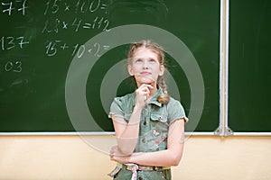 Schoolgirl in the classroom standing at the blackboard solves an elementary example in mathematics