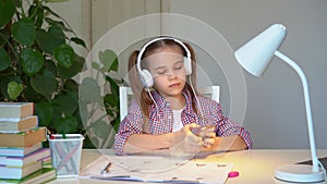 Schoolgirl completes homework puts on headphones and listens to music.