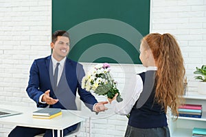 Schoolgirl congratulating her pedagogue with bouquet in classroom. Teacher`s day photo