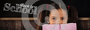 Composite image of schoolgirl covering mouth with book