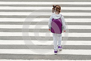 Schoolgirl crossing road on way to school. Zebra traffic walk way in the city. Concept pedestrians passing a crosswalk. Stylish