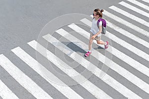 Schoolgirl crossing road on way to school. Zebra traffic walk way in the city. Concept pedestrians passing a crosswalk. Stylish