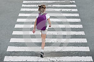 Schoolgirl crossing road on way to school. Zebra traffic walk way in the city. Concept pedestrians passing a crosswalk.  Stylish