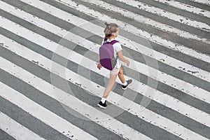 Schoolgirl crossing road on way to school. Zebra traffic walk way in the city. Concept pedestrians passing a crosswalk.  Stylish