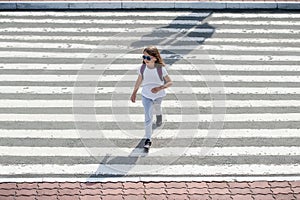 Schoolgirl crossing road on way to school. Zebra traffic walk way in the city. Concept pedestrians passing a crosswalk.  Stylish