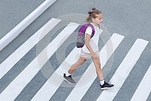 Schoolgirl crossing road on way to school. Zebra traffic walk way in the city. Concept pedestrians passing a crosswalk.  Stylish