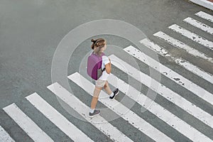 Schoolgirl crossing road on way to school. Zebra traffic walk way in the city. Concept pedestrians passing a crosswalk.  Stylish
