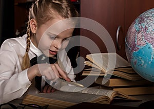 Schoolgirl doing homework, little blonde girl studing at home at the table. children`s education