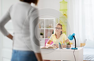 Schoolgirl doing homework and mother entering room