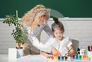 Schoolgirl drawing with teacher. Children from elementary school study at draw lesson. Teacher and little students