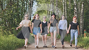 Schoolgirl friends are walking outside the city along a forest road.