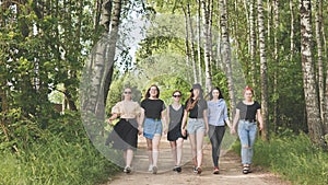 Schoolgirl friends are walking outside the city along a forest road.