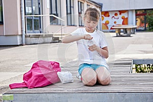 Schoolgirl girl drinks fresh mineral water from a bottle in the schoolyard. Take a break from school. Quenching thirst,
