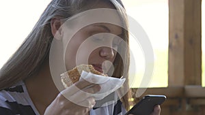 Schoolgirl girl having lunch with a sandwich and a burger holding a smartphone in her hands. School break fast food