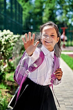 a schoolgirl girl in a white shirt with a backpack at school shows her palm five
