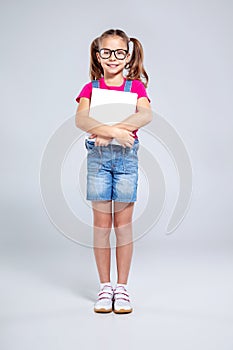 Schoolgirl in glasses with backpack and textbook on the gray background