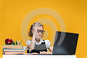 Schoolgirl in glasses raising hand sitting at laptop during online lesson. Distant School Learning.
