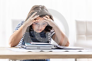 Schoolgirl in glasses tries to comprehend study materials holding her head by both hands