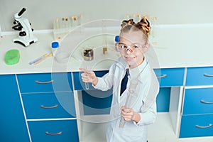 Schoolgirl in goggles holding reagents in flasks in chemical lab