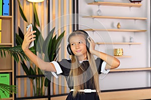 A schoolgirl in headphones listens to music and takes a selfie with her phone.