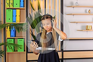 A schoolgirl in headphones listens to music and takes a selfie with her phone.