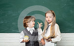 Schoolgirl helping pupils studying at desks in classroom. Teacher and child. Blackboard background. Little children at