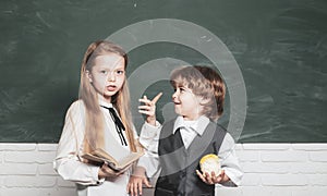 Schoolgirl helping pupils studying at desks in classroom. Teacher and child. Blackboard background. Little children at