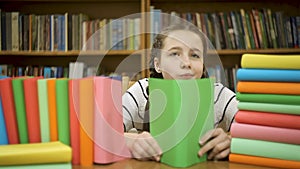 A schoolgirl is hiding behind a book in the library.