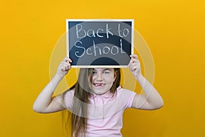 Schoolgirl holding a tablet in her hands with the inscription Back to school on a yellow background