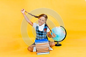 Schoolgirl isolated on yellow background with globe. little girl in school uniform sitting on a yellow background, reading a book