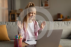 Schoolgirl Making Video Call Waving Hello To Laptop At Home