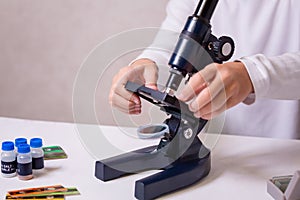 A schoolgirl with a microscope examines chemicals in test tubes, conducts experiments. The concept of coronavirus