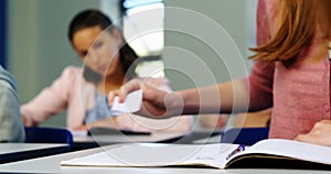 Schoolgirl passing chit to her classmate during exam in classroom