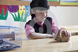 Schoolgirl petting pet rabbit in classroom