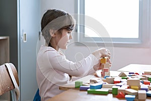 Schoolgirl playing with colorful toy blocks while sitting at table in class room at Elementary school. Educational and creative