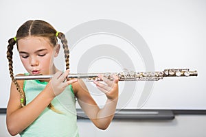 Schoolgirl playing flute in classroom