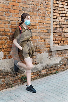 Schoolgirl poses against a brick wall in the backyard of the school, wearing a protective mask on her face from a coronavirus