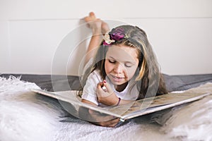 The schoolgirl is reading. Little girl reading a book in the bedroom on the bed. Education and hobbies of children