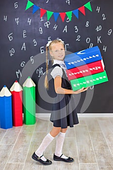 The schoolgirl in school uniform with books and textbooks is on a light gray background. Back to school. The new school year. photo