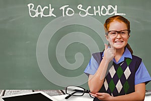 Schoolgirl showing thumb up sign while back to school written on chalkboard